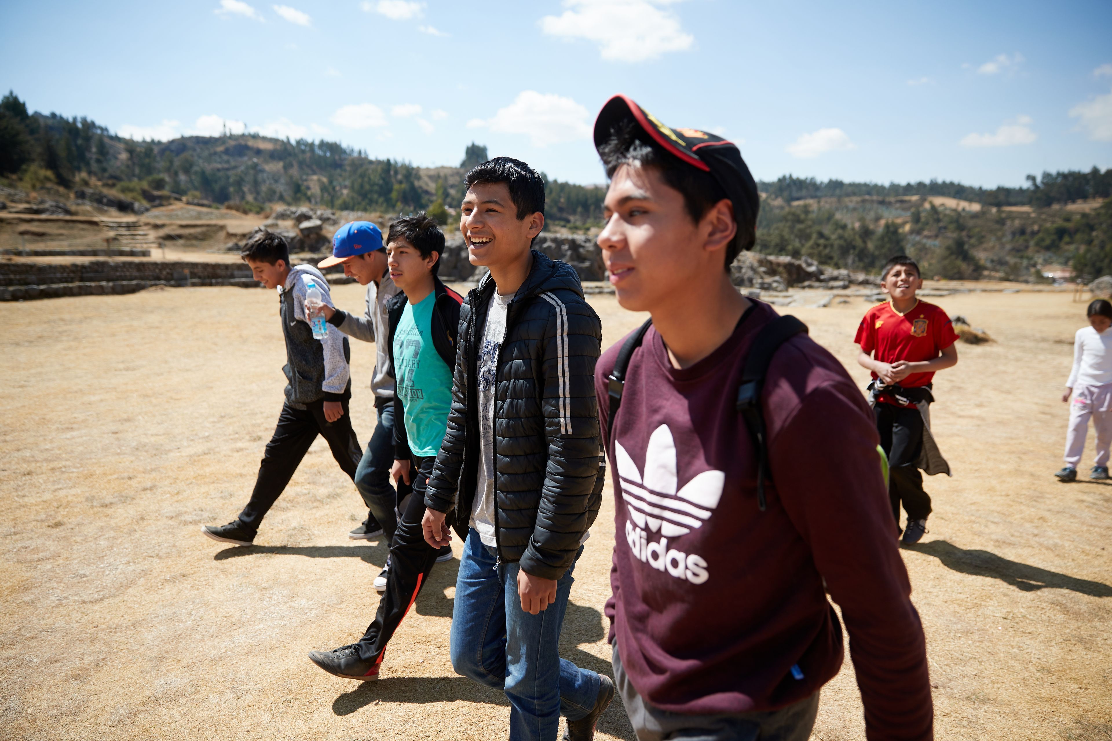 Various young men are hiking together. They appear to be on a campout. They talk and laugh as they walk. This is in Cusco, Peru. 