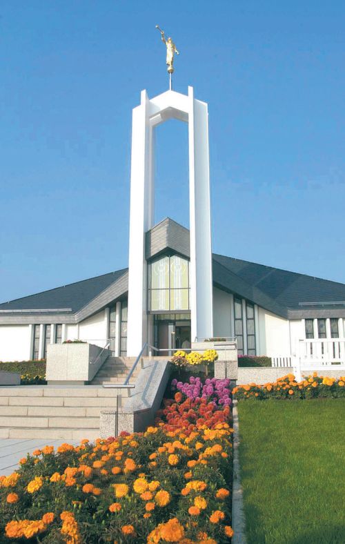 The entrance and spire of the Freiberg Germany Temple, with large, colorful flowers in bloom in the flower beds near the door.
