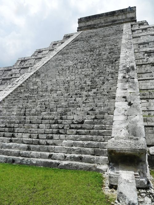 A large stone pyramid with a long row of stairs leading to the top, with a partially cloudy sky seen overhead.