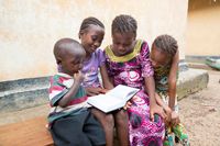 Various children, possibly siblings, sit outside together. They are all looking at copies of scriptures. Together they are reading and studying together. This is in Sierra Leone, Africa.