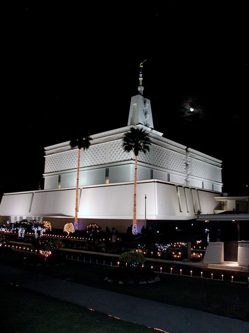 A front and side view of the Mexico City Mexico Temple at night, lit up with lights for the Christmas holiday, with a moon in the sky.