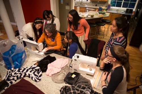 A small group of sister missionaries gathered around a kitchen table learning to sew together.