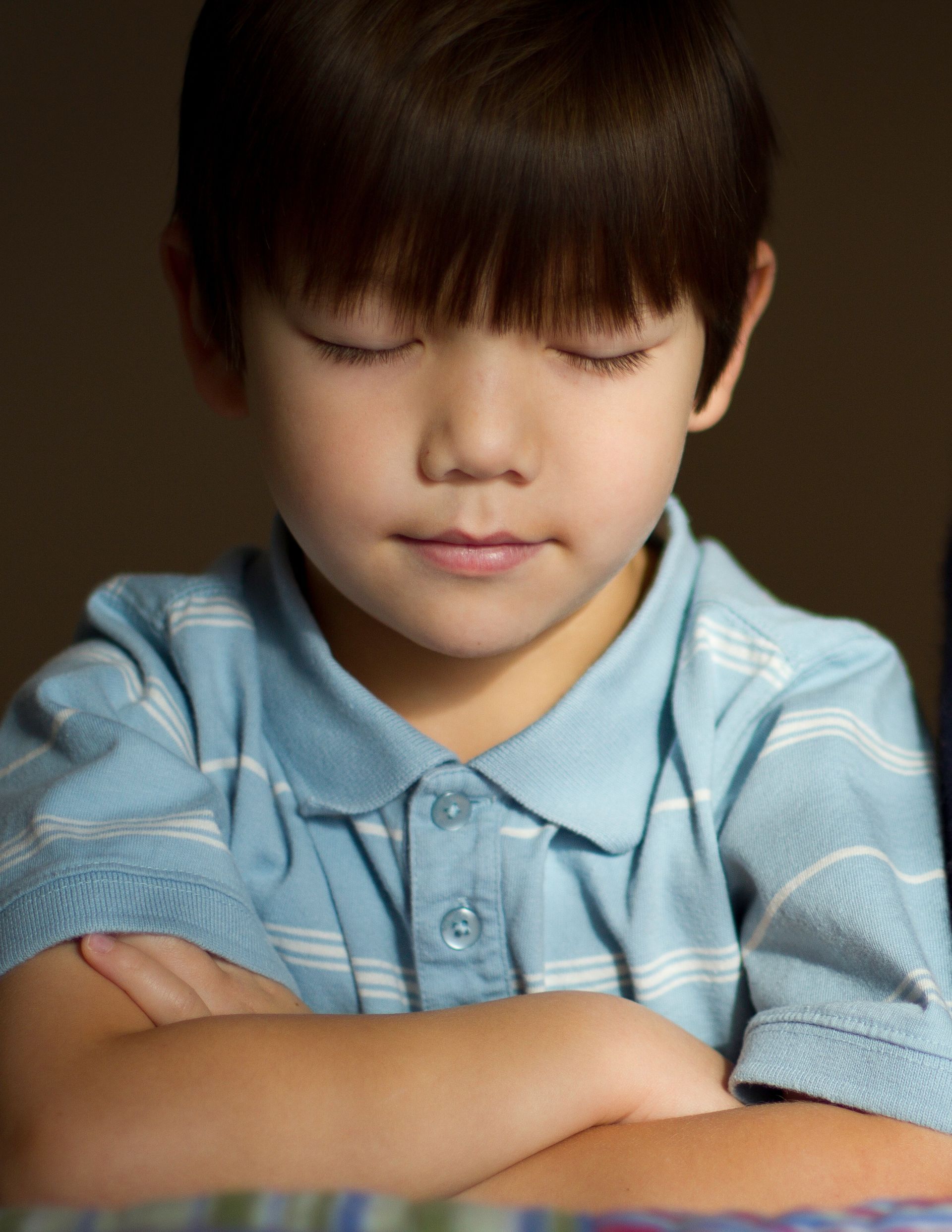 A boy kneeling by his bed with his eyes closed and arms folded in prayer.