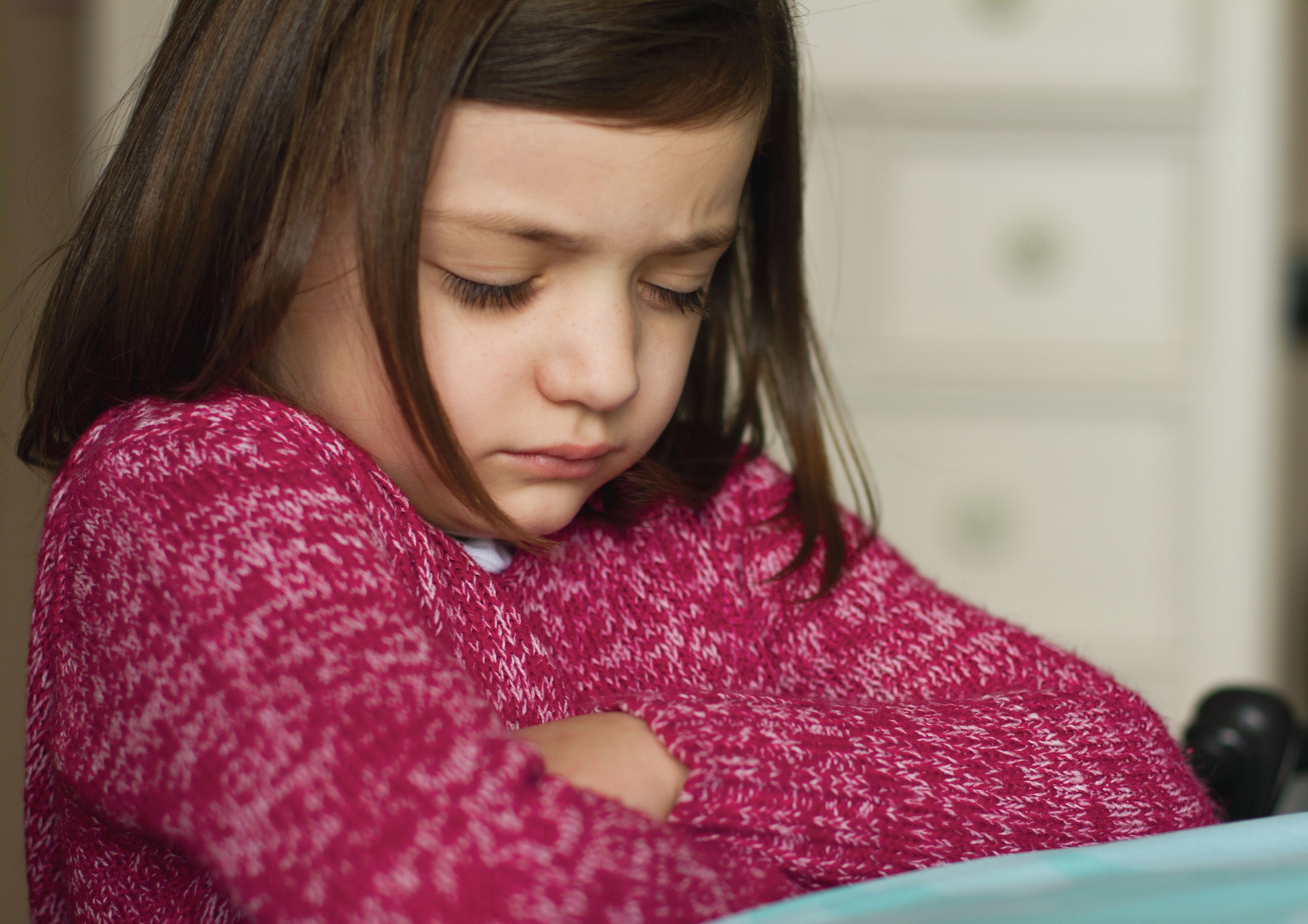 A young girl in a pink sweater folds her arms and prays.