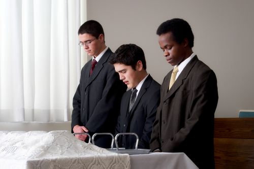 Three young men close their eyes and pray to bless the sacrament in front of them.