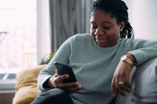 Smiling young woman using a mobile phone while sitting on a couch.