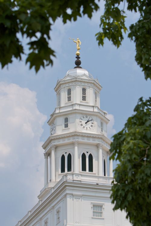 The spire on the Nauvoo Illinois Temple, with the angel Moroni seen between the green leaves of trees in the foreground.