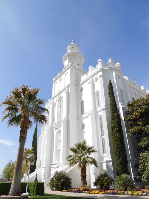 The front of the St. George Utah Temple, with a view of the spire, entrance, and grounds with trees.