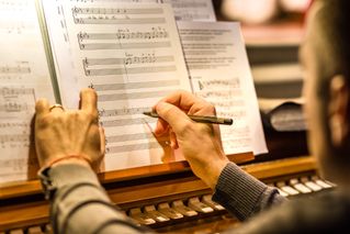 An man sitting at an organ composing music - He is writing notes of  sheet music