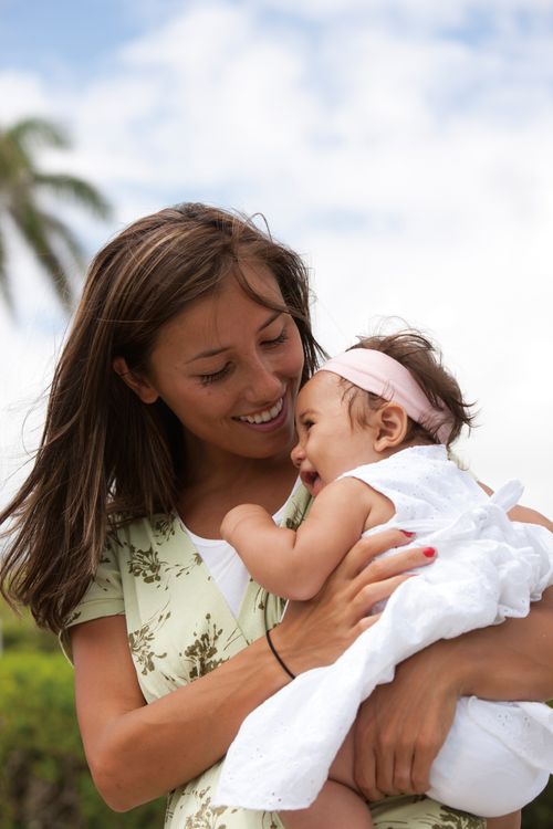 A mother in Hawaii holds her baby daughter in her arms while outside.