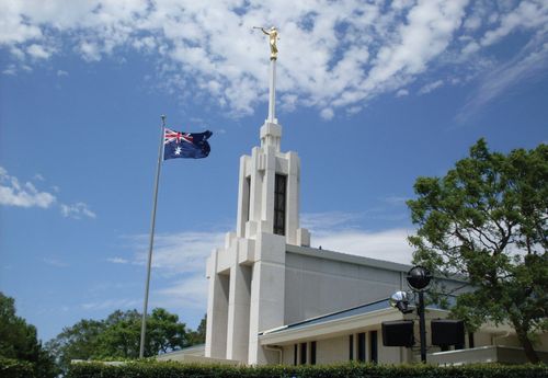 A side view of the front of the Sydney Australia Temple, with the Australian flag flying on the grounds.