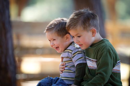 A boy in a dark green shirt sitting with his arm around his younger brother in a striped shirt.