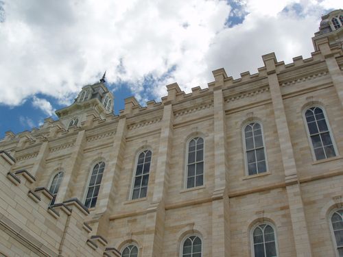 A close-up view of one side of the Manti Utah Temple exterior—walls, windows, and spire—with a blue sky and clouds above.