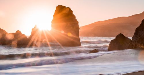 raggi di sole attraverso una formazione rocciosa su una spiaggia