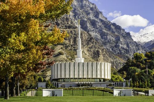 The north side of the Provo Utah Temple, with a view of the grounds around the temple and the mountains behind.