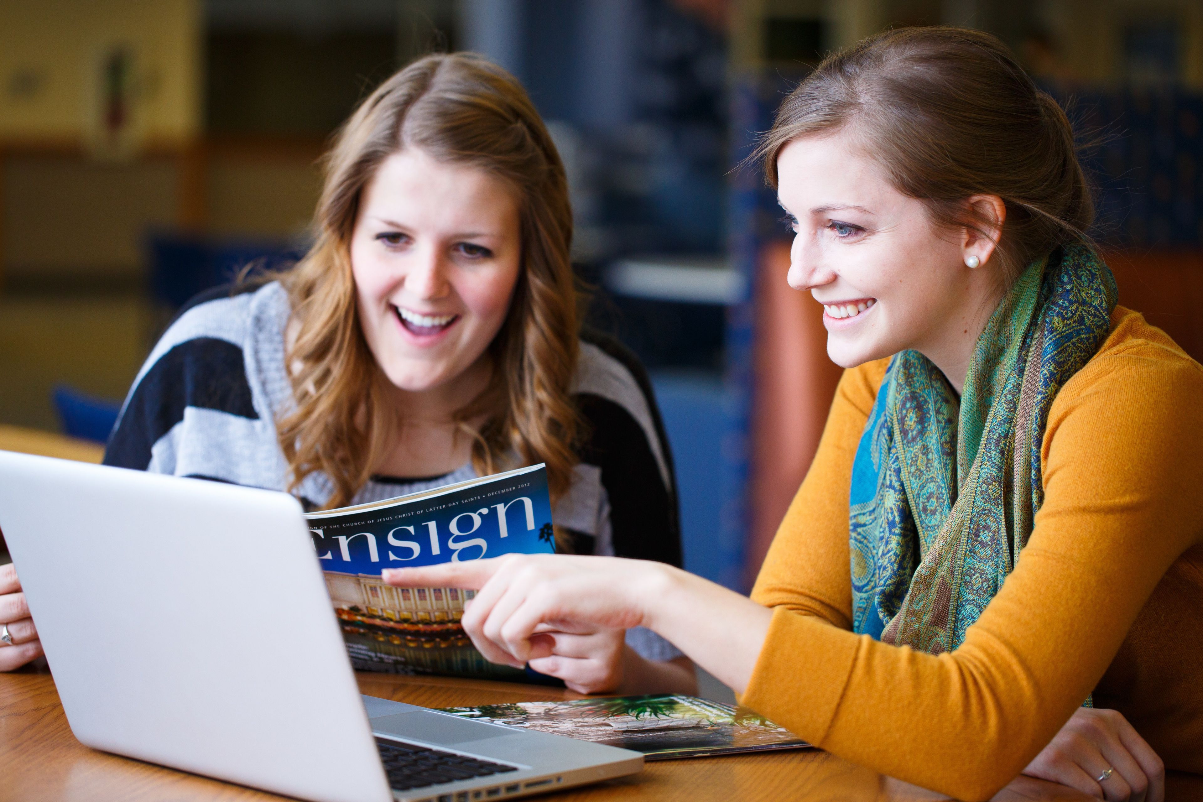 Two young women look at a laptop and read out of the Ensign.