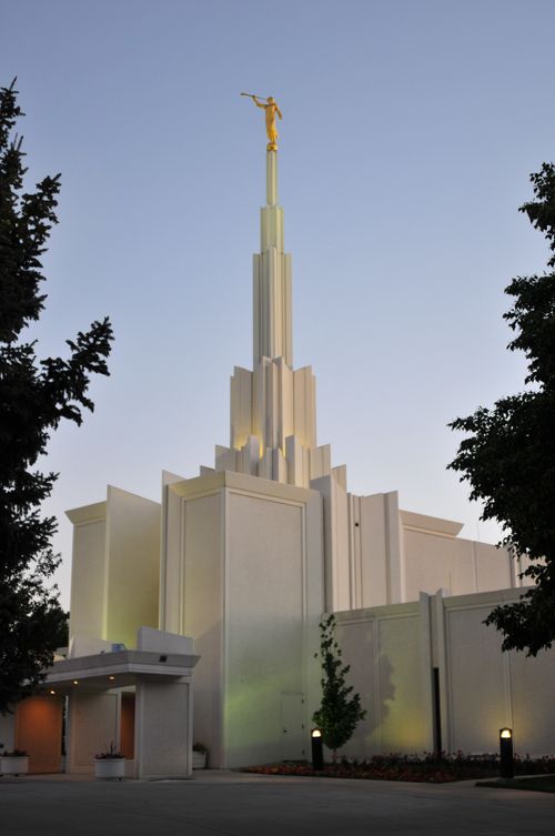 A front side view of the Denver Colorado Temple in the evening, with large trees on either side.