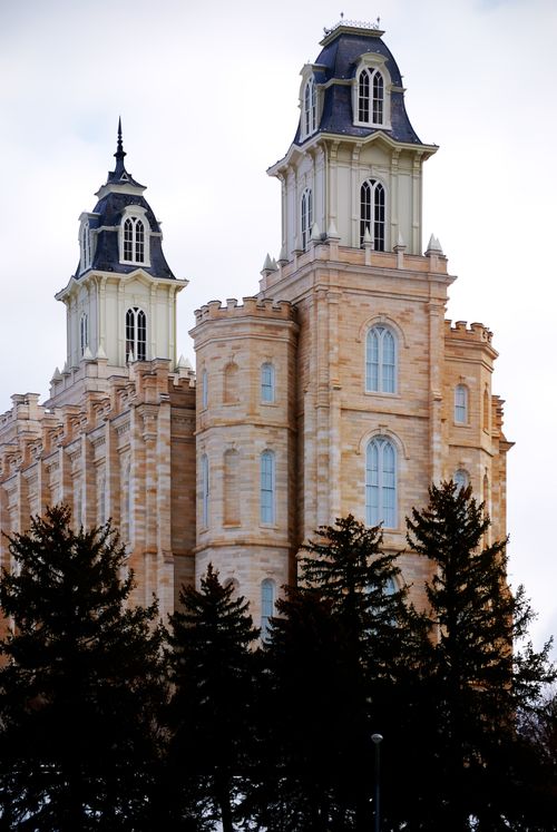 The Manti Utah Temple’s front side exterior and spires are seen over the top of trees.