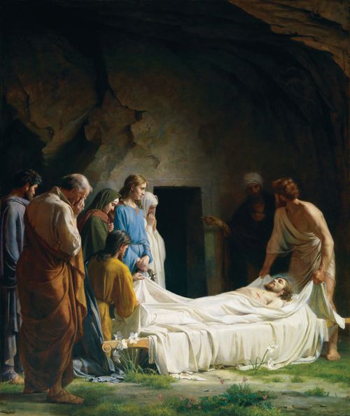 Christ’s friends wrapping His body in white linens to prepare Him to be placed into a tomb, which is seen in the background.