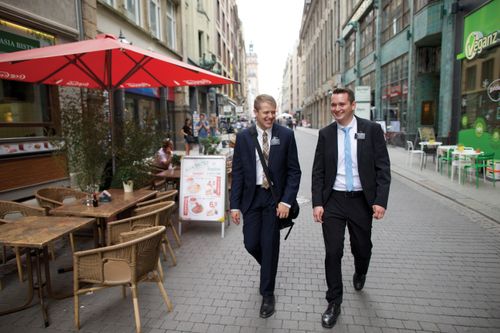 Two young elder missionaries in dark suits walk down a city street.
