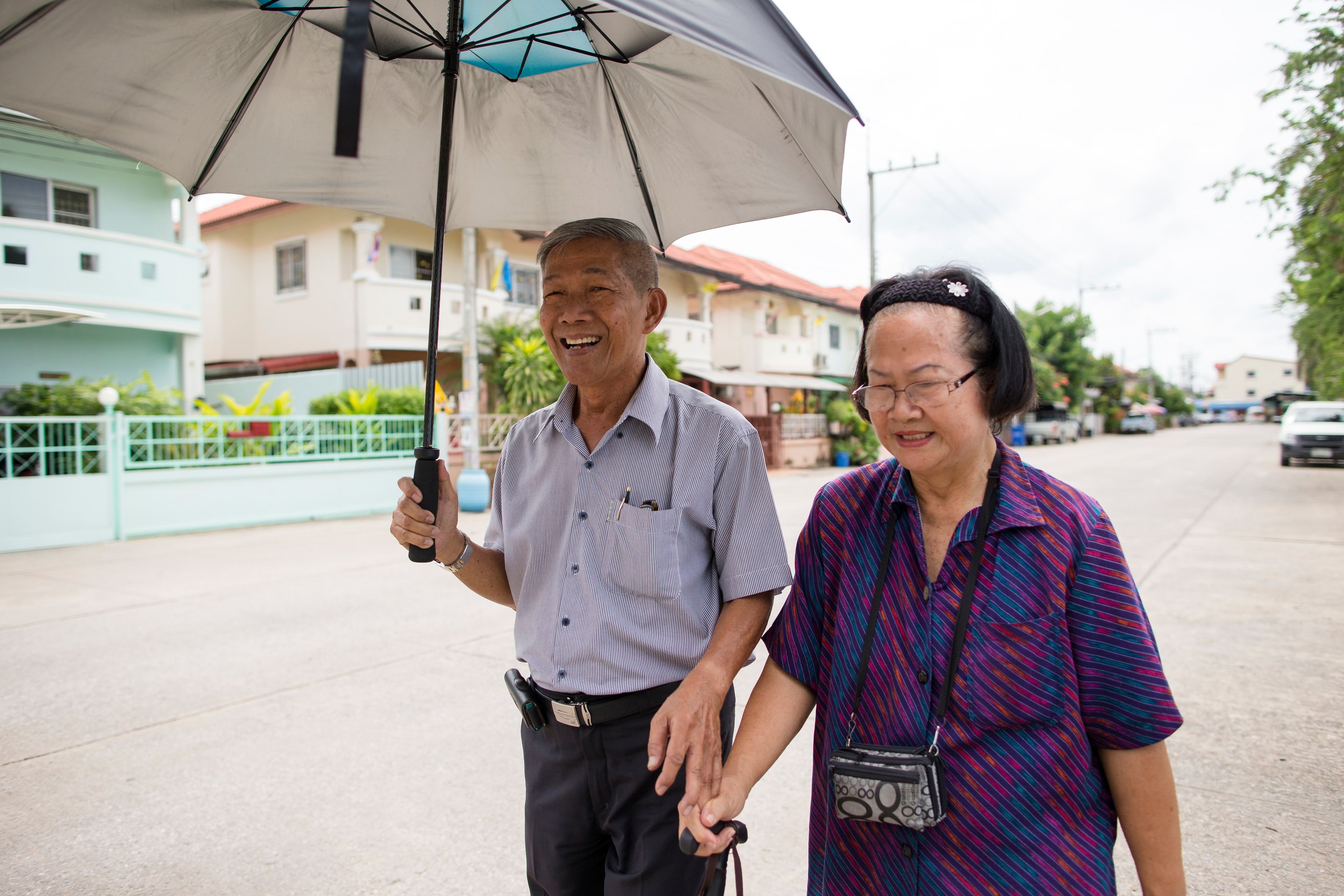 A man holding an umbrella and walking next to his wife in Thailand.  