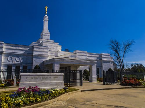 A daytime photograph of the front of the Baton Rouge Louisiana Temple, showing the temple’s sign and the flower beds in full bloom.