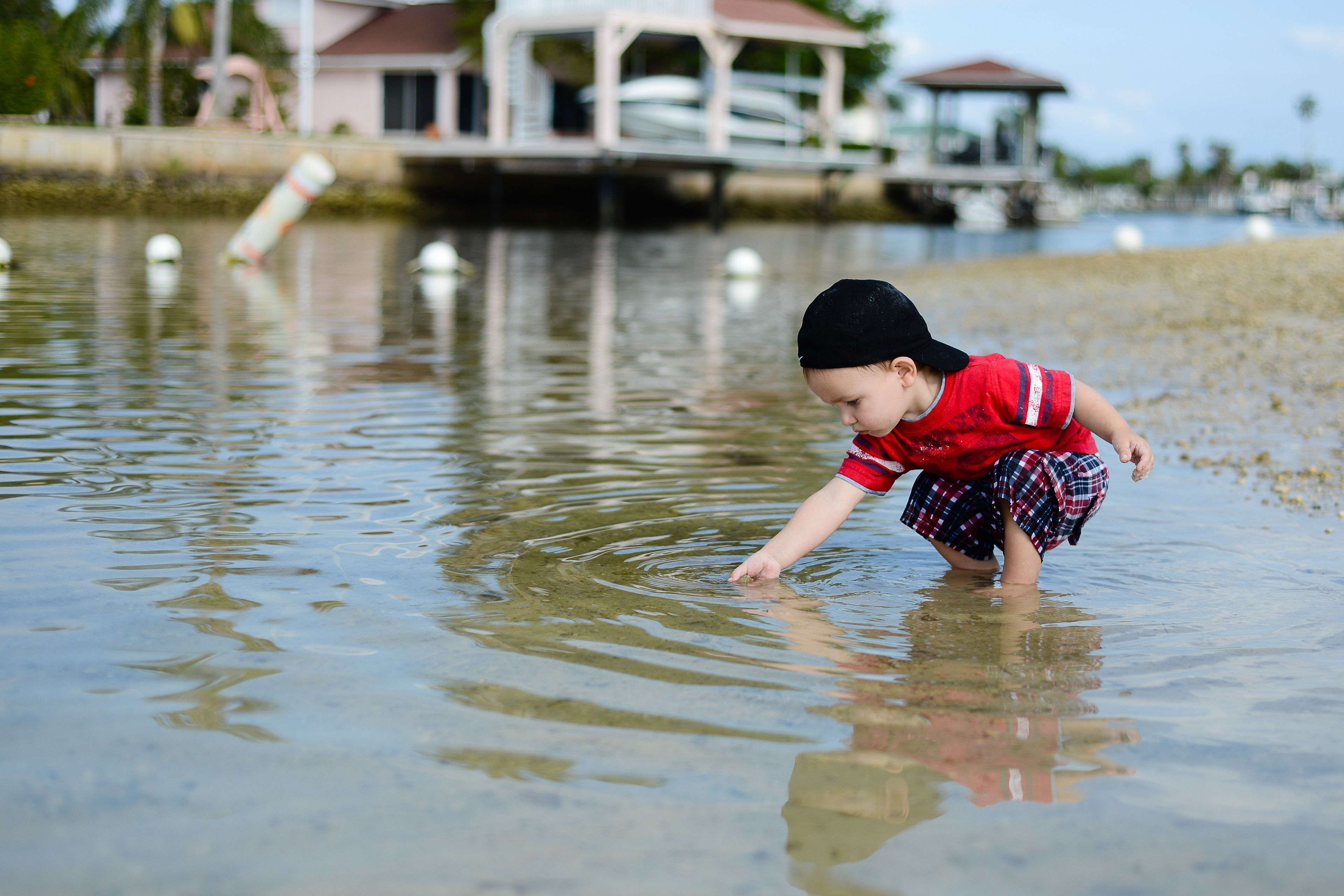 A toddler boy reaches his hand down into the water.