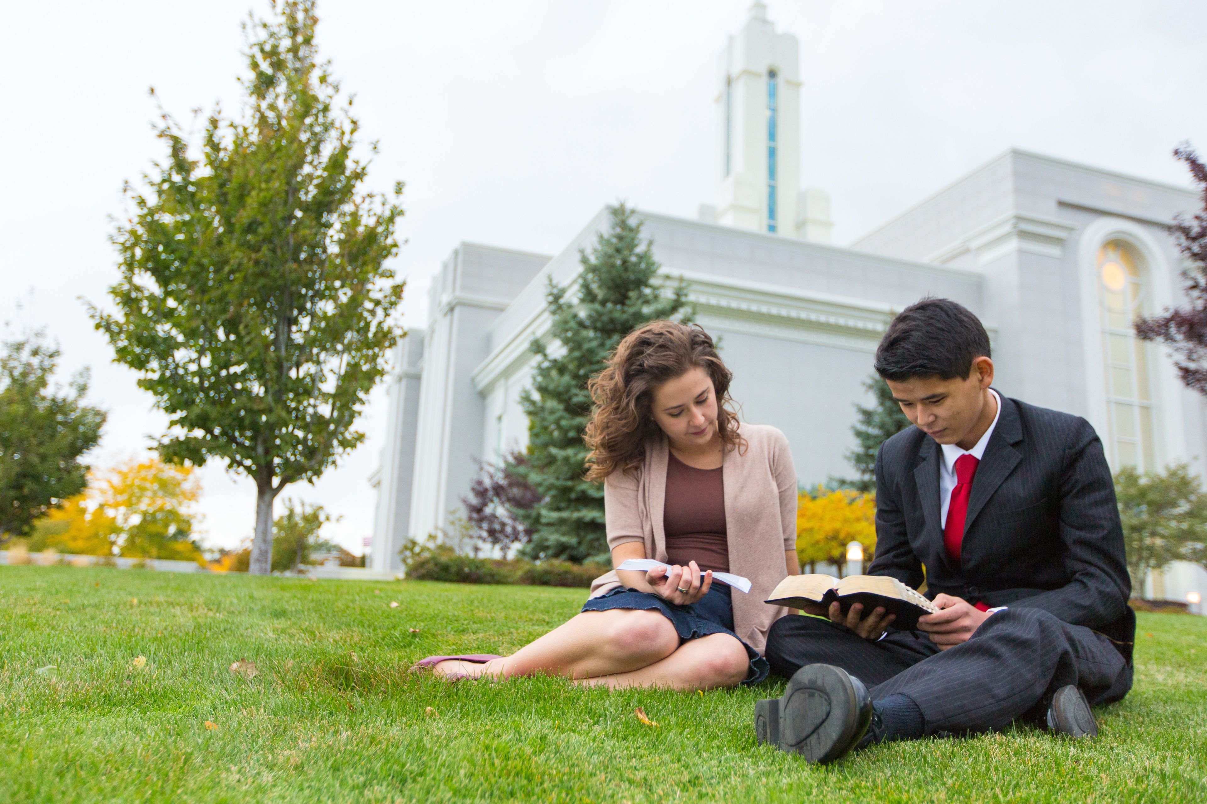 A young man and woman reading scriptures on the lawn at the Mount Timpanogos Utah Temple.