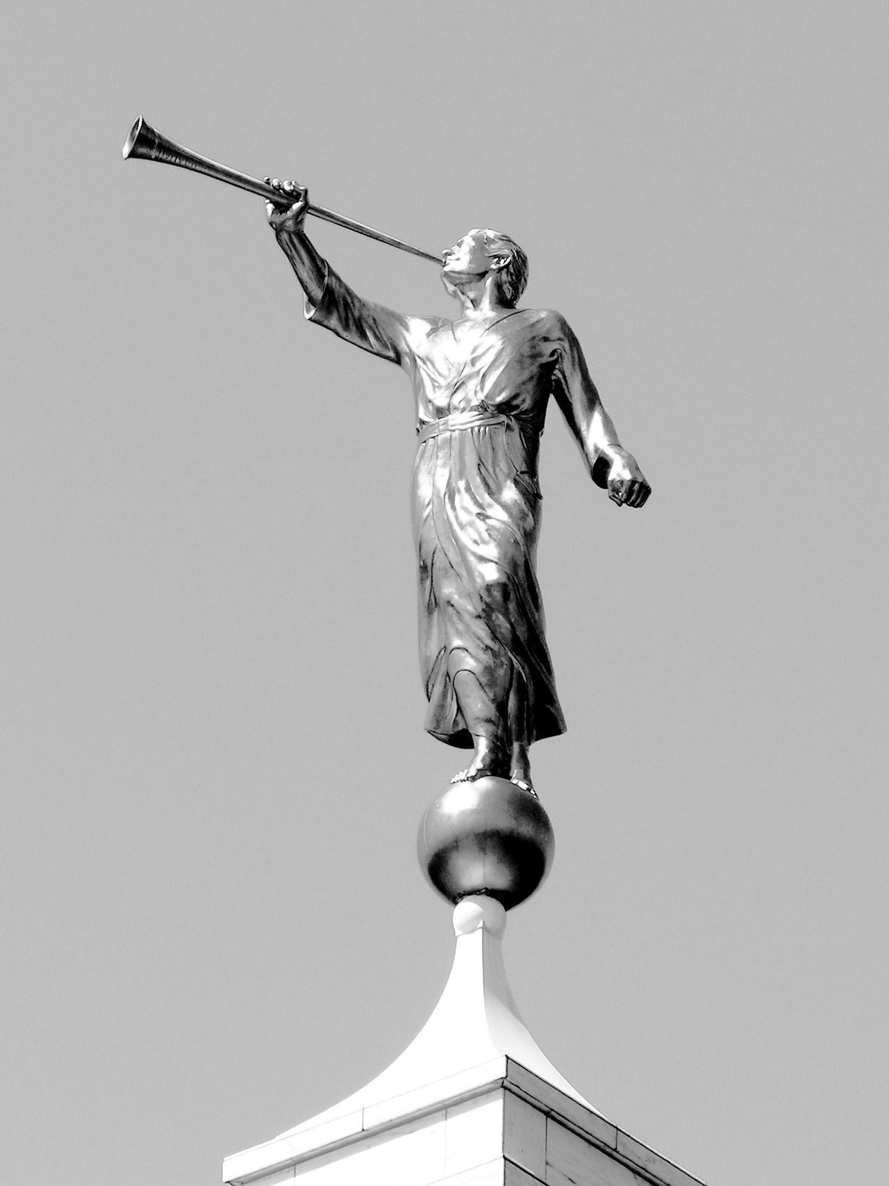 A close-up black-and-white view of the angel Moroni statue on top of a temple spire.