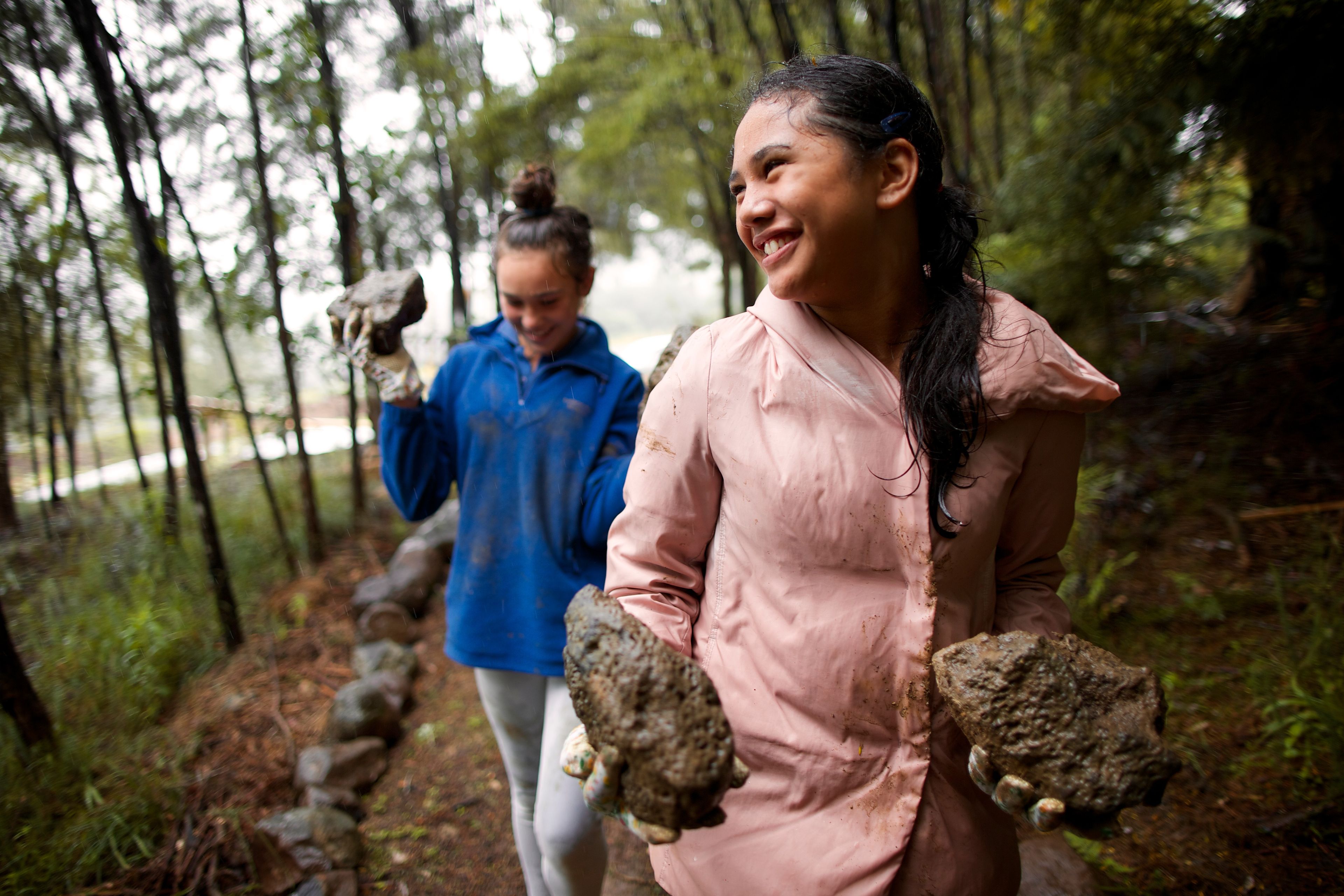 Two young women help lay rocks down to line a path.  