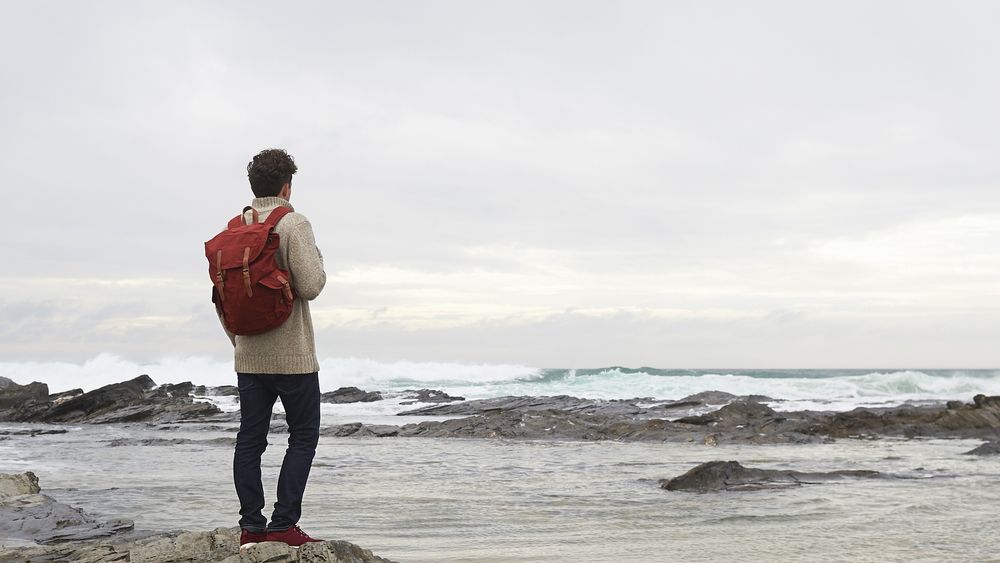 Male hiker looking out to sea from coastal rocks