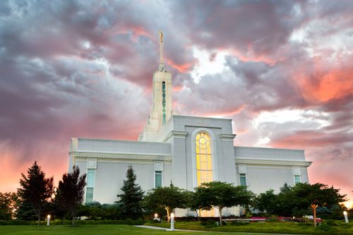 A view of the Mount Timpanogos Utah Temple reflecting the colors of the sunset, with the lights on inside and outside of the temple.