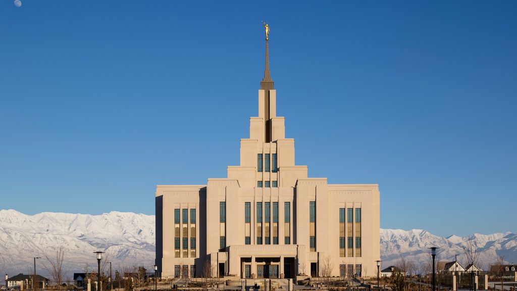 Exterior image of the Saratoga Springs Utah Temple taken during the day. There are mountains with snow are in the background.