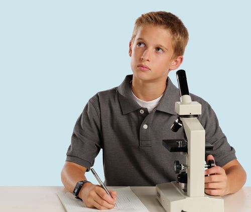 Young man using a microscope and writing on a pad of paper.