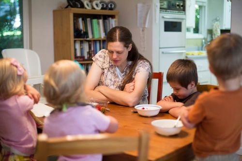 A mother folds her arms and prays at the breakfast table with her four children.