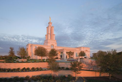 The entire San Antonio Texas Temple in the evening, with the sunset reflecting off of the temple and with a view of the entrance, stairs, and grounds around the temple.