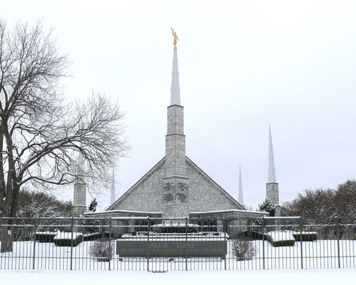 The front of the Dallas Texas Temple on a gray winter day, covered in snow, with a large bare tree near the entrance.