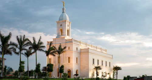 Barranquilla Colombia Temple. This image takes in the temple and temple grounds. The sun appears to be setting off in the distance. Lights are coming on outside and around the temple.