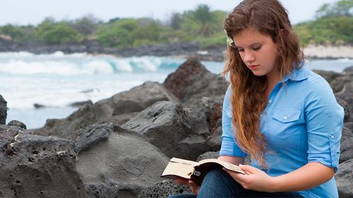 girl reading scriptures by the ocean