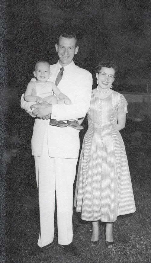 Grant Heaton holds an infant while standing next to Luana Heaton, all smiling.