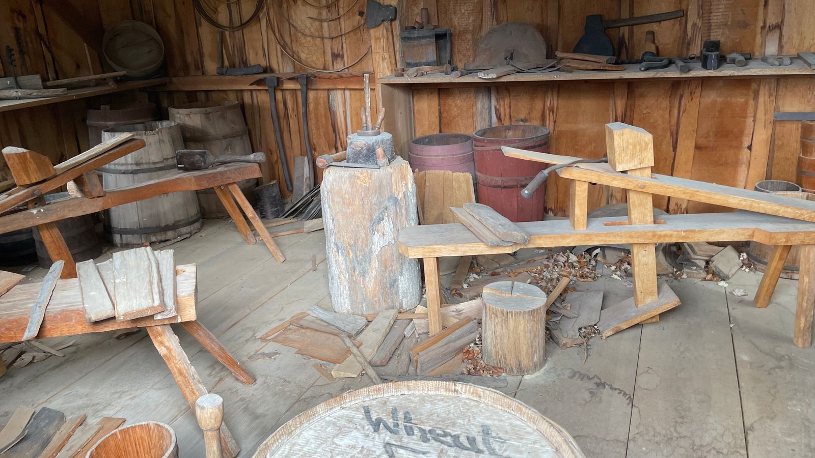 Interior of a wood shop with small pieces of wood, wooden benches, and hand tools strewn about.