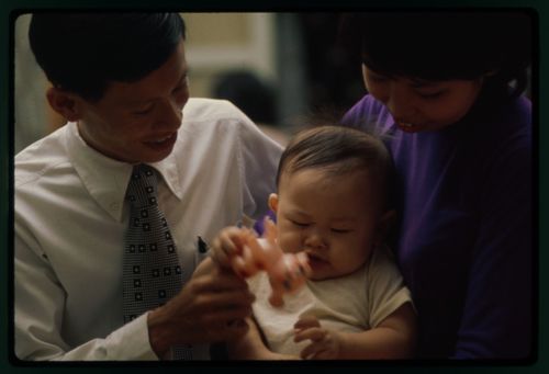 Nguyen Van The and Le My Lien look down at their infant son, who plays with a toy.