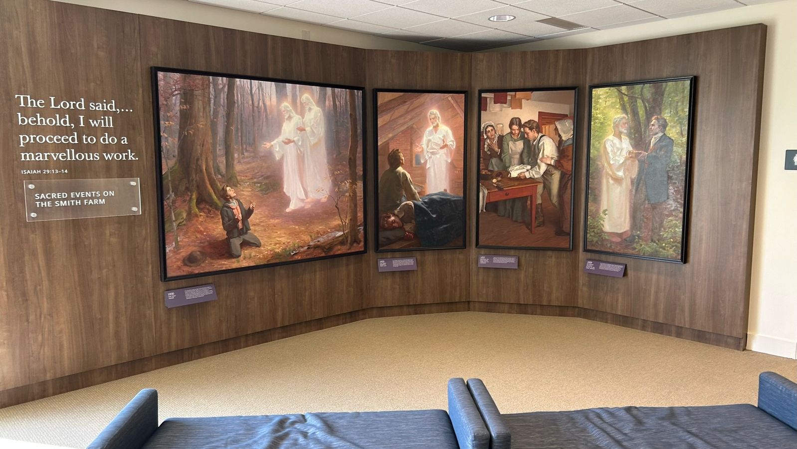 An exhibit wall with a featuring four paintings of an angelic visiros and Joseph Smith. Benches sit in front of the display. A title on the right reads "The Lord said . . . behold, I will proceed to do a marvellous work." This passage is from Isaiah 29 in the Old Testament.