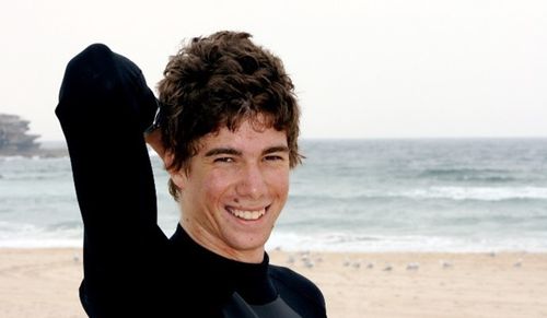 Blake McKeown smiles at the camera while wearing a wetsuit on the beach.