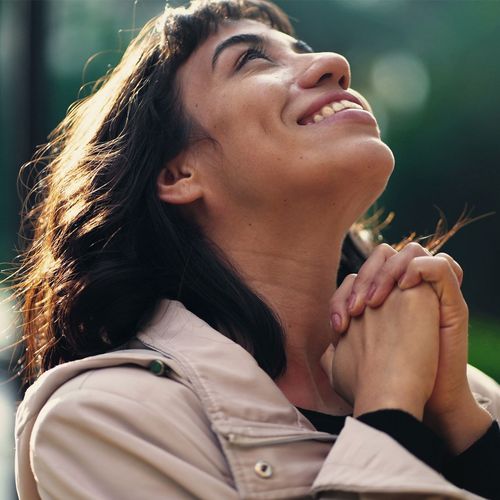 a woman clasping her hands and smiling at the sky