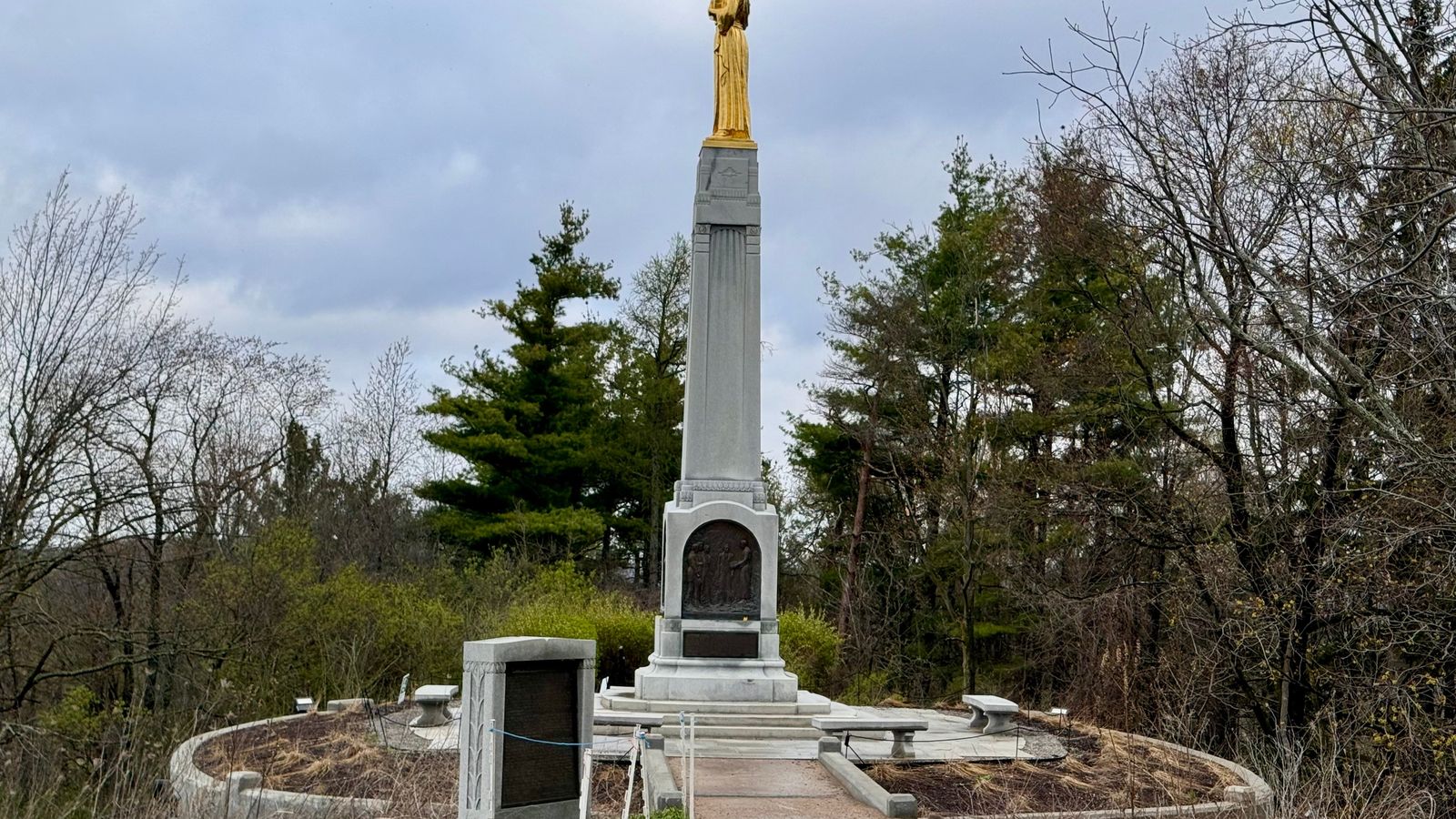 Side view of a tall stone piller with a large gold angel on top.